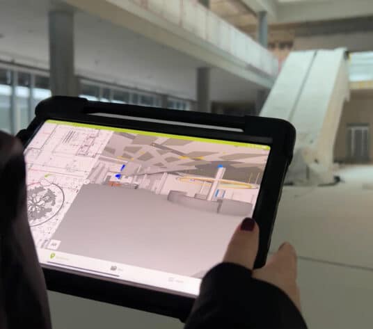 Visualisierung auf Tablet und Baustelle Haupteingang KSB-Neubau mit Treppenlift im Hintergrund.