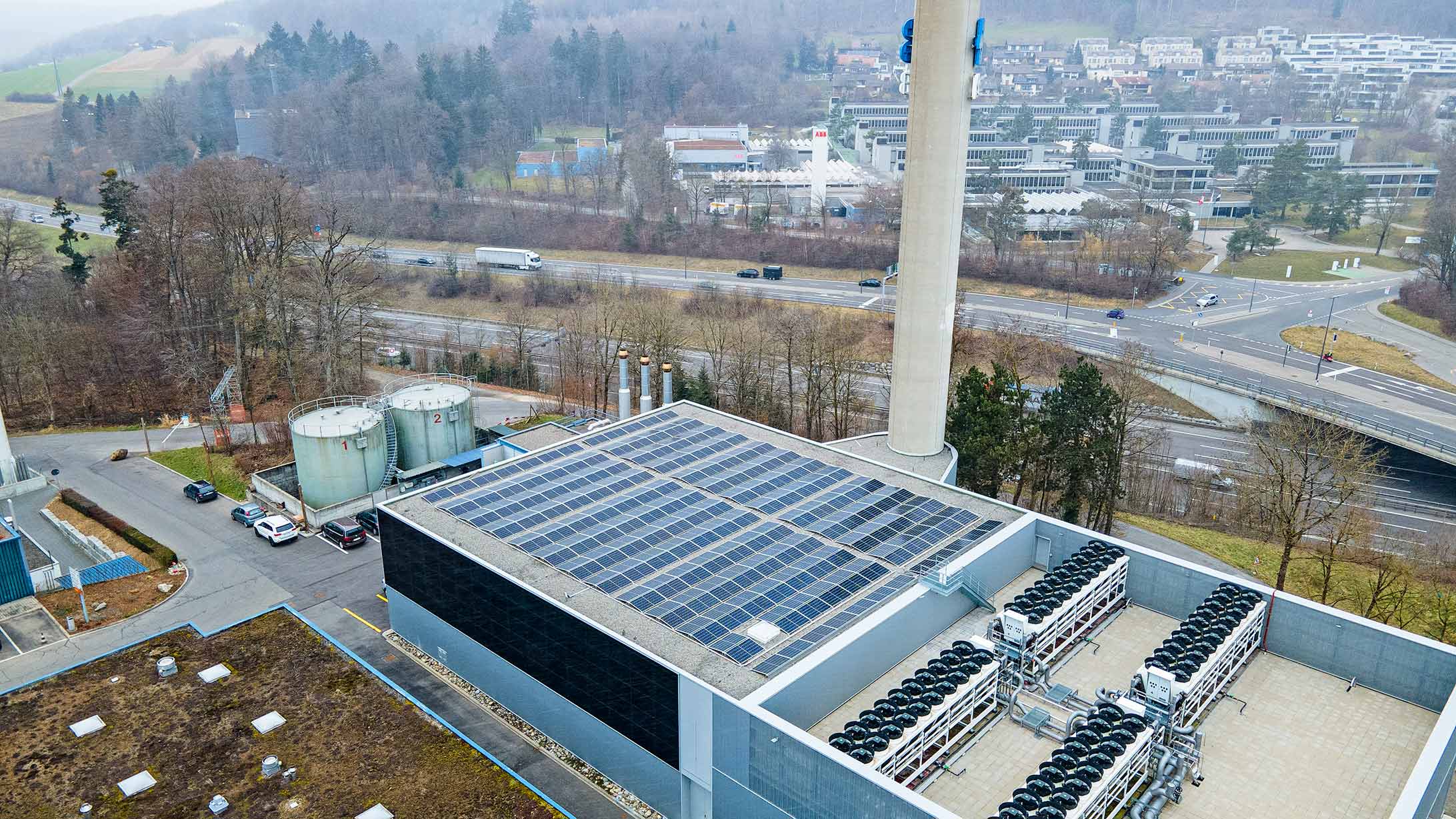 Drohnenbild der Energiezentrale Gesundheits-Campus KSB mit Kamin und Photovoltaikanlage auf dem Dach, Autobahn A1 im Hintergrund.